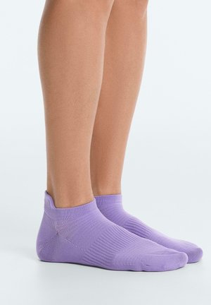 Benen met korte, geribde lila enkelsokken op een effen lichte achtergrond, zij aan zij staand.