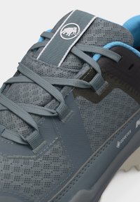 Szaro-niebieski but trekkingowy z siateczkową cholewką, szarymi sznurowadłami, metką Gore-Tex i logo mamuta na języku.