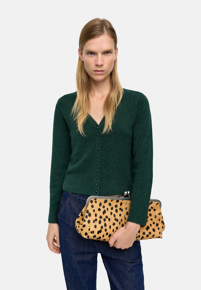 Zielony, dzianinowy kardigan z dekoltem w kształcie V i zapięciem na guziki, w połączeniu z tanowym kopertówką z czarnym wzorem w panterkę. Ciemne dżinsy.