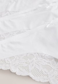 Bijeli materijal s rubom od čipke u valovitom obliku koji prikazuje cvjetne uzorke, naglašen sitnim detaljima s mašnicama. Mekana tekstura s detaljnim dizajnom.