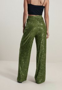 Pantalon large en sequins verts avec une surface texturée et une taille élastique. La finition brillante souligne la forme et le mouvement du vêtement.