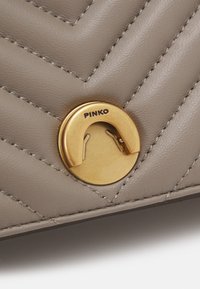 Dettaglio di una borsa in pelle grigia con texture a trapunta a zig-zag, hardware dorato con logo "PINKO" e evidenti rifiniture della cucitura.