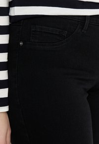 Svarta denimjeans med en slim fit, femficksdesign och en liten framficka. Har en silverfärgad knappaccent. Tyget ser slätt ut.