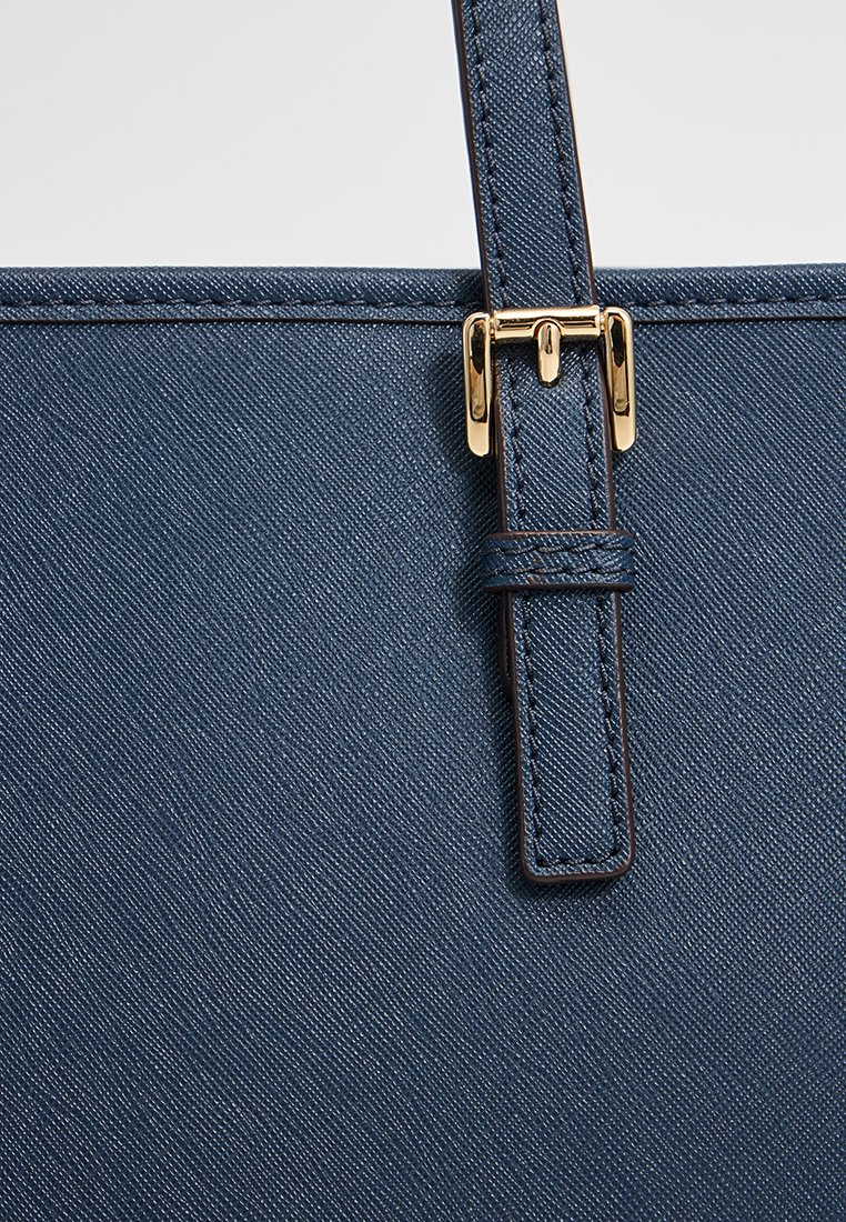 Sac fourre-tout bleu foncé en tissu texturé, avec une boucle en métal doré et des détails cousus sur la bandoulière.