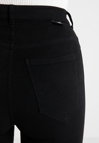 Jeans de mezclilla negros de cintura alta con una textura suave, que cuentan con un bolsillo trasero y un detalle de costura sutil.