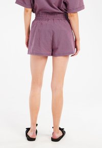 Pantaloni corti a scacchi viola con vita elastica, caratterizzati da una vestibilità ampia e un design informale. Indossati con sandali neri senza fibbie.
