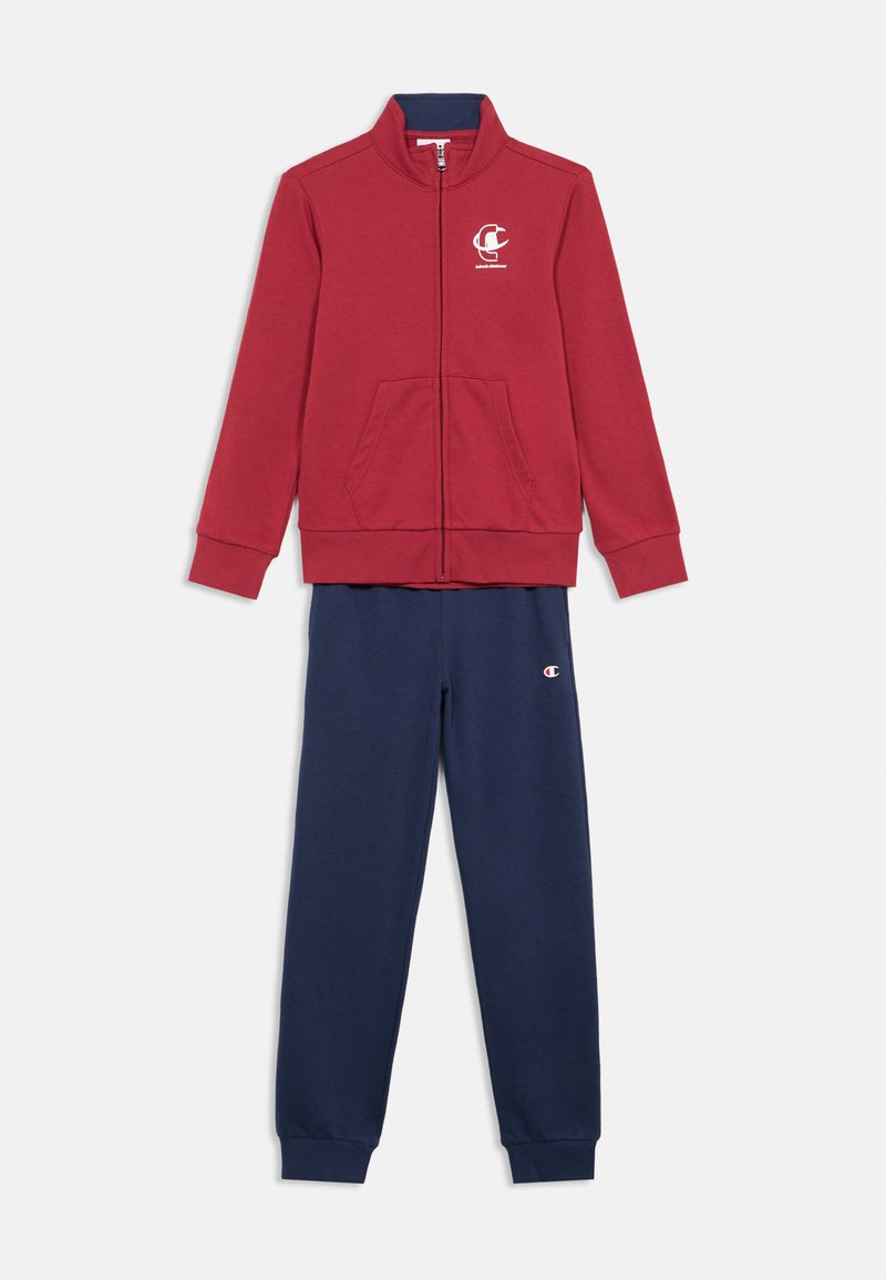 Κόκκινο μπουφάν με φερμουάρ και τσέπες, μαζί με μπλε ναυτικό φούτερ με ελαστικές μανσέτες. Και τα δύο είναι κατασκευασμένα από μαλακό ύφασμα· το μπουφάν έχει λογότυπο στο στήθος.