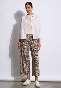 Un pantalon large à imprimé léopard beige associé à un haut crème clair et à une chemise blanche. Le look est complété par des baskets blanches.