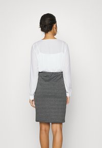 Blusa branca de mangas longas com um tecido suave e semi-transparente, combinada com uma saia lápis cinza quadriculada ajustada, com um padrão texturizado.