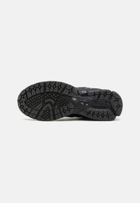 Semelle de chaussure de sport noire avec un motif texturé, dotée de profonds sillons et d'éléments de traction pour une meilleure adhérence et stabilité.