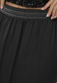 Jupe noire avec une taille élastique texturée ornée d'accents métalliques. La jupe possède un tissu doux et fluide avec de légers plis.