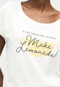 Λευκό πουκάμισο που φοριέται από άτομο με στρογγυλή λαιμόκοψη, με κίτρινο γραφικό λεμονιού και κείμενο «Αν η ζωή σου δίνει λεμόνια, φτιάξε λεμονάδα!»