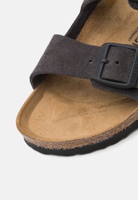 Sandalo in suede nero con plantare in sughero e soletta marrone texturizzata. Presenta una larga fascia e una fibbia nera regolabile per una vestibilità sicura.