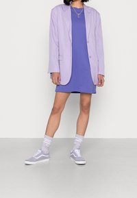 Fioletowy oversize'owy żakiet, niebieska sukienka t-shirtowa i pasujące fioletowe trampki. Teksturowane skarpetki w paski dopełniają całość.