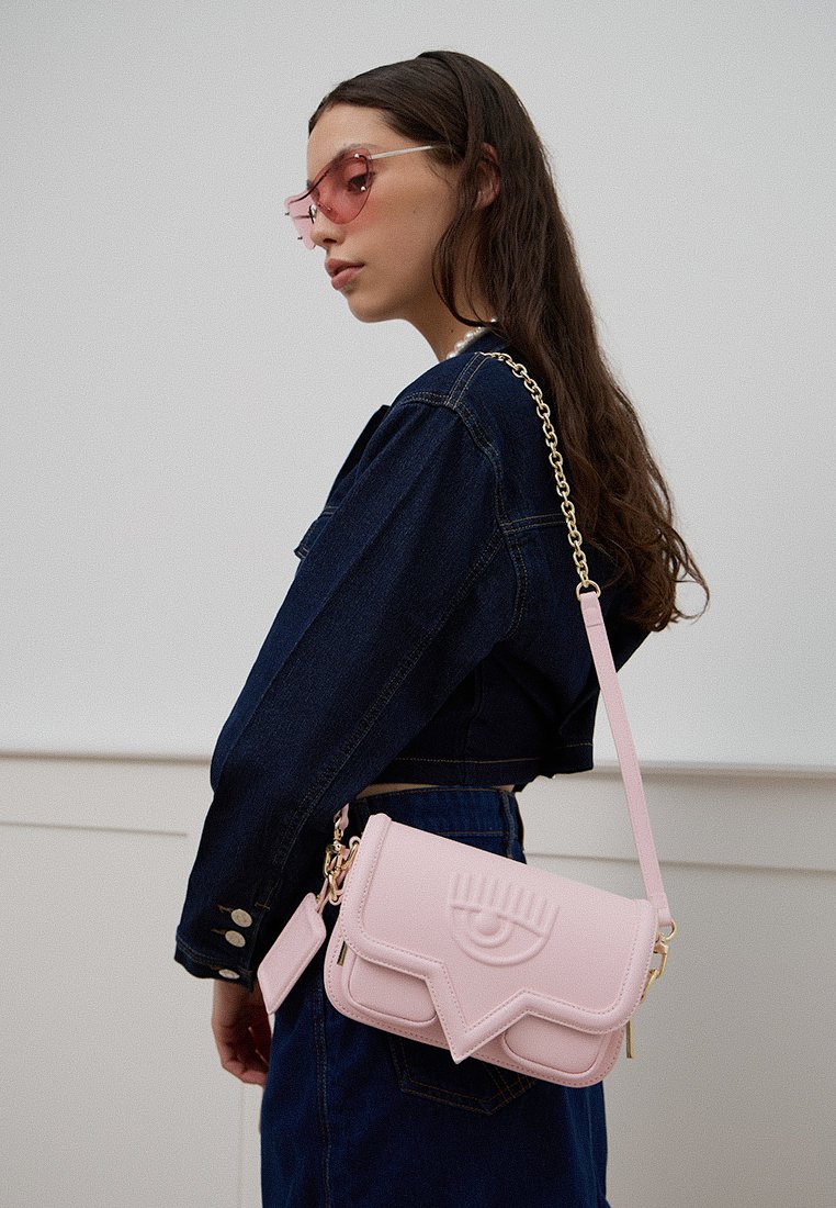 Różowa torebka crossbody z faux skóry z klapą z wytłoczonym motywem oka, złotymi akcentami i odczepianym łańcuszkiem.