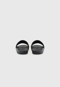 Black slide sandals with open back and wide straps. Textured footbed and smooth sole. Minimalist design with no visible branding.