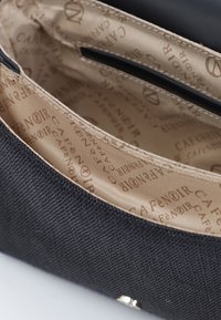 Svart texturerad tyghandväska inuti med en beige foder som visar ett upprepat "Cafenoir" logomönster och en slät metallstängning.