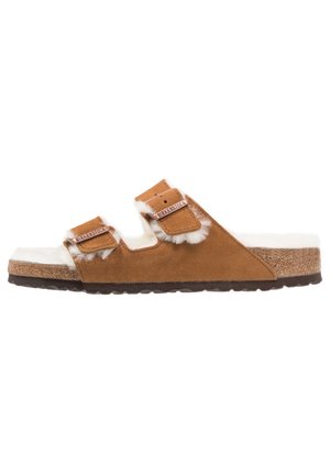 Bruine suède sandalen met twee verstelbare banden, zachte faux fur voering en een kurken voetbed. Zijaanzicht toont de gegoten rubberen zool.