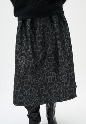 Schwarz-grauer Leopardenmuster-Midirock, getragen mit schwarzen kniehohen Lederstiefeln und einem schwarzen, flauschigen Pullover.