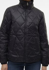 Veste noire matelassée avec un col montant, dotée d'une fermeture éclair frontale et de poignets élastiques. Tissu lisse, légèrement réfléchissant avec des motifs en forme de losanges.