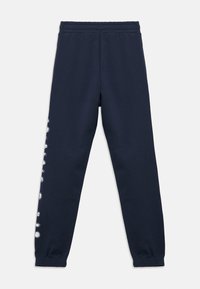 Σκούρο μπλε παντελόνι φόρμας με ελαστική μέση και μανσέτες, διακοσμημένο με κάθετο λευκό σχέδιο κατά μήκος της εξωτερικής πλευράς του αριστερού ποδιού.