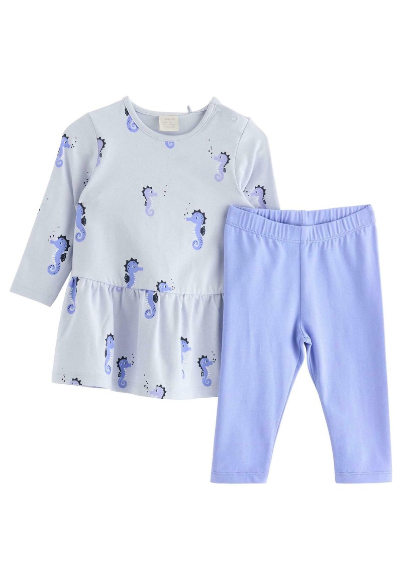 Jasnoniebieska bluzka z długim rękawem z nadrukiem konika morskiego i falbaniastym dołem, zestawiona z jednolitymi legginsami w kolorze lawendy. Materiał z bawełny, miękka faktura.