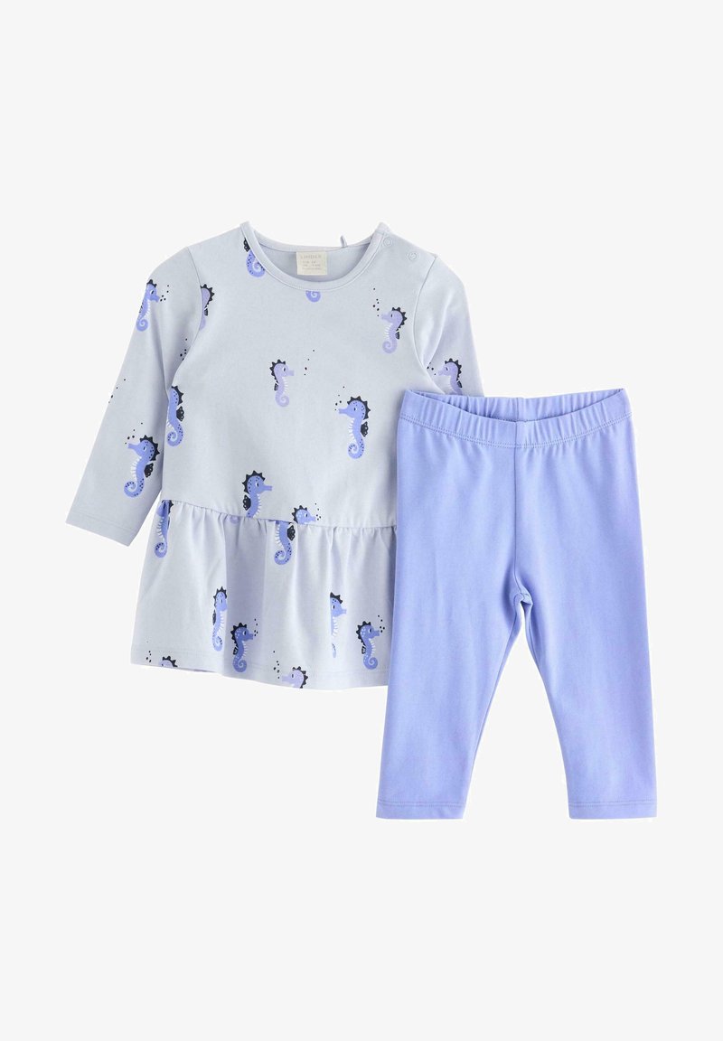 Jasnoniebieska bluzka z długim rękawem z nadrukiem konika morskiego i falbaniastym dołem, zestawiona z jednolitymi legginsami w kolorze lawendy. Materiał z bawełny, miękka faktura.