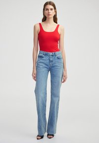 Top de tirantes rojo ajustado combinado con jeans acampanados de color azul claro. Los jeans presentan una cintura alta, un diseño clásico de cinco bolsillos y un ligero desgaste.