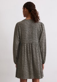 Czarna sukienka w kwiaty z długimi rękawami, okrągłym dekoltem i marszczonym stanem. Tkanina ma biały wzór kwiatowy na całej powierzchni.