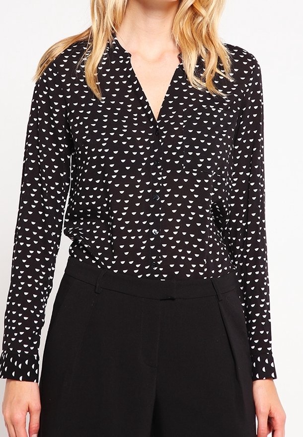 Blouse noire à manches longues avec une fermeture boutonnée sur le devant, présentant un motif triangulaire blanc et un tissu doux et léger. Coupe ajustée.
