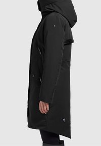 Cappotto lungo nero con cappuccio, tasche con zip e tessuto texture. Presenta un logo e un design frontale piatto. Cuciture a punto e una silhouette aderente.