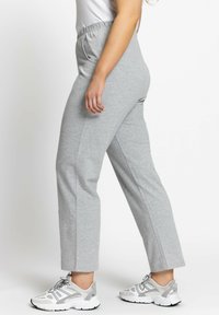 Šedé tapered tepláky s elastickým pasem, prezentované vedle bílých tenisek s šedými akcenty. Hladká textura a uvolněný design.