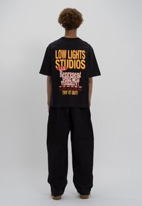 Black oversized t-shirt featuring colorful graphic text on the back: "LOW LIGHTS STUDIOS," "Represent yourself visually!" and other text details.