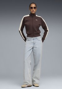 Καφέ ζακέτα με φερμουάρ και κρέμ ριγές, σετ με ανοιχτό μπλε τζιν παντελόνι φαρδιάς γραμμής και μπεζ παπούτσια με καφέ σόλες. Αξεσουάρ: γυαλιά ηλίου.