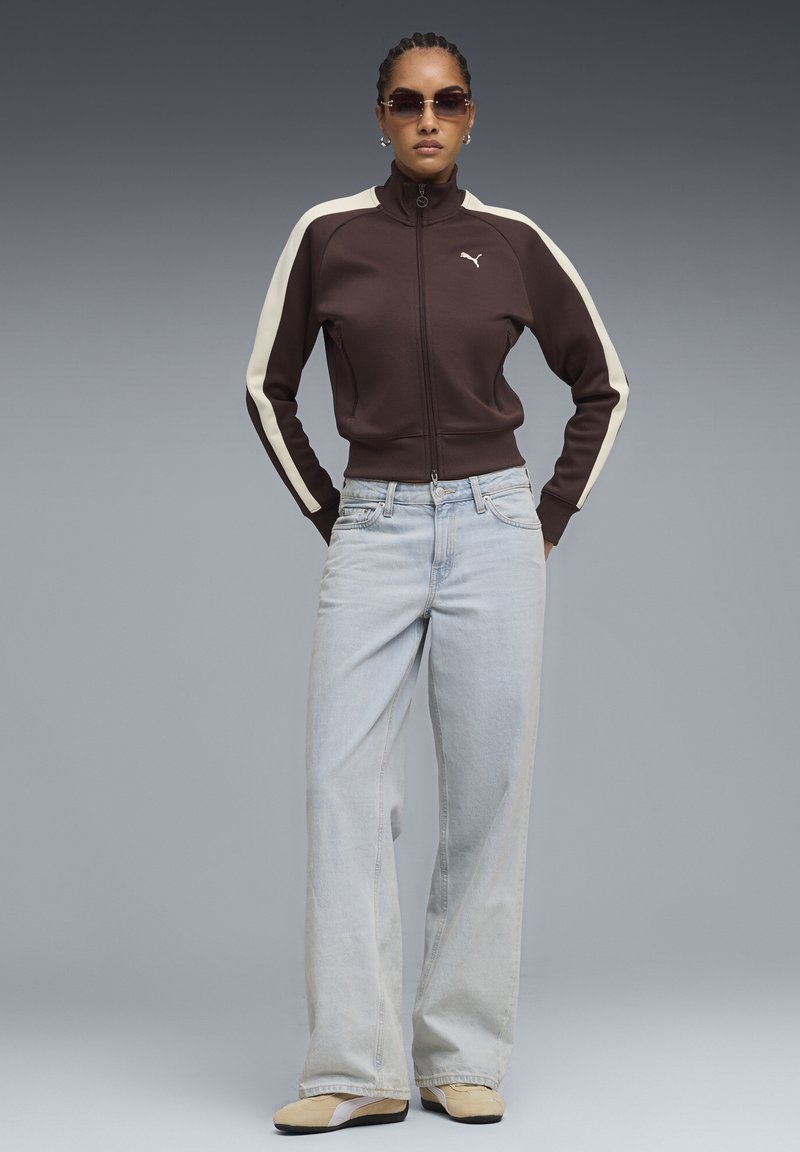 Καφέ ζακέτα με φερμουάρ και κρέμ ριγές, σετ με ανοιχτό μπλε τζιν παντελόνι φαρδιάς γραμμής και μπεζ παπούτσια με καφέ σόλες. Αξεσουάρ: γυαλιά ηλίου.