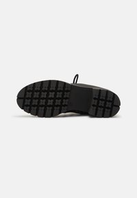 Suela negra texturizada con surcos profundos para tracción, que presenta un área de talón moldeada y un componente superior suave y flexible.