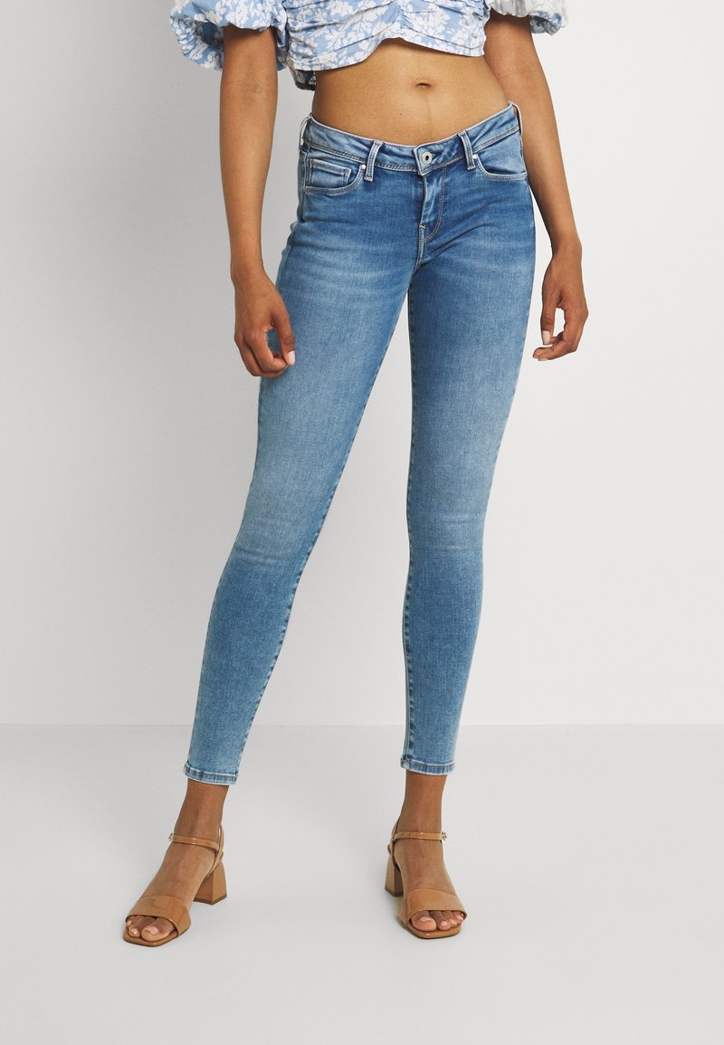 Jeans ajustados de color azul claro, confeccionados en denim, que presentan una cintura de altura media, diseño de cinco bolsillos y un ligero desgastado. Combinados con tacones de bloque beige.