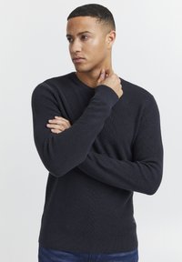 Mørk marineblå strikket sweater med lange ærmer, ribbet tekstur og rund halslinning. Har et logomærke på kanten.