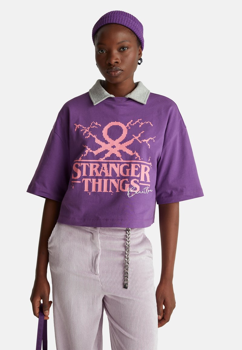 Camiseta púrpura corta con cuello gris y gráfico rosa de "Stranger Things" con diseño de pulpo. Complementada con pantalones lilas a rayas.