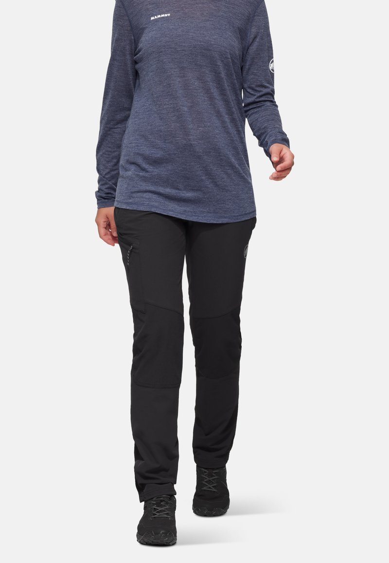 Personne portant une chemise bleue à manches longues et un pantalon de plein air noir avec des genoux renforcés et des chaussures de randonnée noires marchant vers l'avant.