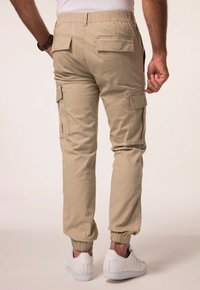 Beige cargo bukser med elastisk talje og manchetter. Har to baglommer og sidelommer. Sammen med hvide sneakers.