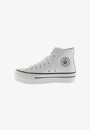 White high-top sneakers made of smooth leather, featuring a round toe, black accents, and a circular logo patch on the outer side.