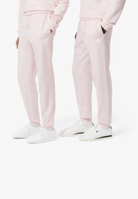 Roze trainingsbroek met elastische tailleband en zijzakken, met het witte Lacoste-logo. Gecombineerd met witte sneakers met groene details.