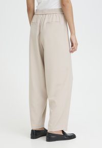 Beige wide-leg trousers with an elastic waistband, two back pockets, and a smooth texture, paired with black loafers.