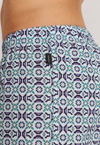 Shorts pour homme en tissu léger, ornés d'un motif géométrique bleu, vert et violet. Taille élastique avec un détail de marque.
