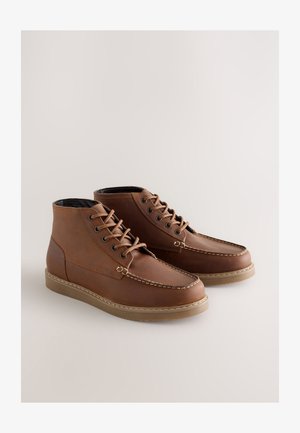 Brune læderankelstøvler med kontrastsyet, rund tå, flad gummisål og snøredesign. Har sort indvendigt for.