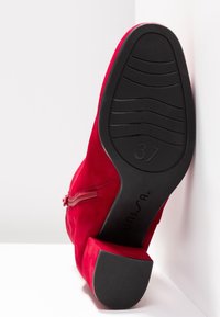 Bottine en cuir suédé rouge avec semelle en caoutchouc noire, talon bloc, fermeture éclair latérale et taille 37 visible sur la semelle.
