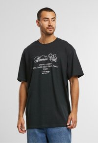 Black cotton t-shirt with a relaxed fit, short sleeves, and white printed text featuring "Winners Club" and an address in Paris.