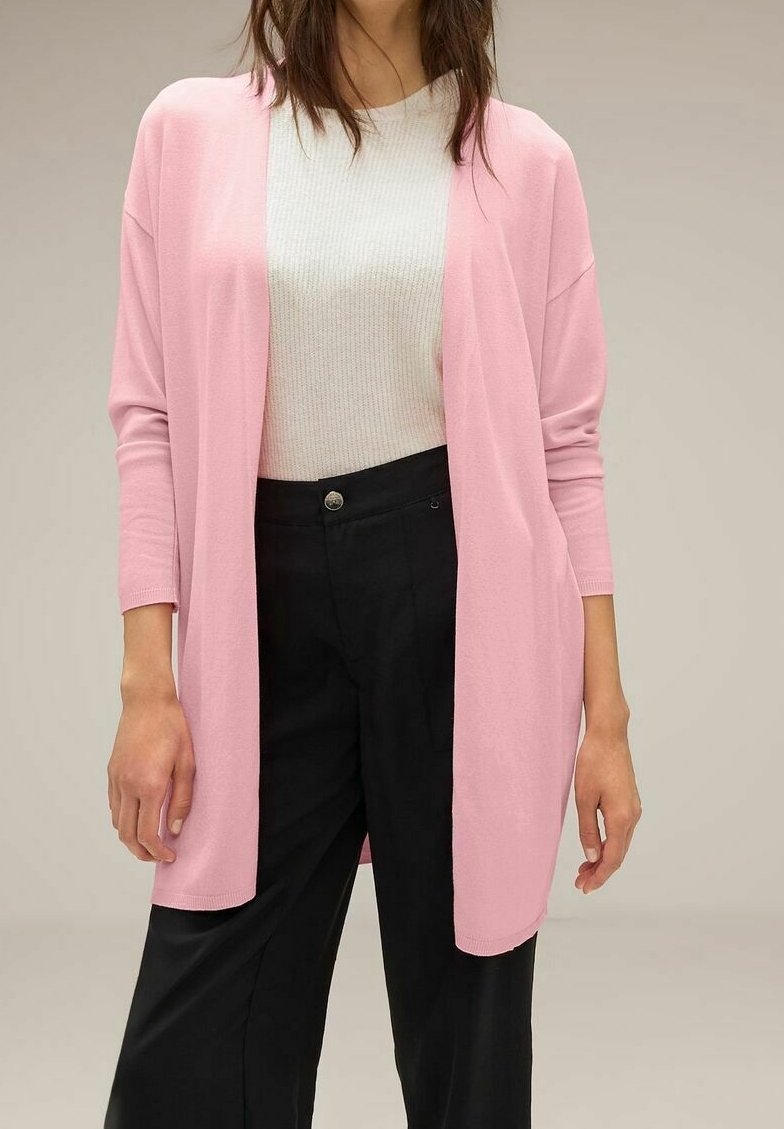 Ljusrosa cardigan med långa ärmar, öppen framsida, mjuk textur, bärs över en vit ribbad skjorta och svarta byxor.
