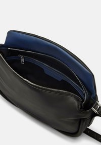 Czarna skórzana torba na ramię z niebieskim wnętrzem, kieszeniami na zamek błyskawiczny i gładką fakturą. Posiada srebrny zamek błyskawiczny oraz regulowany pasek.